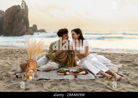 Amate le coppie romantiche che fanno un picnic sulla spiaggia sabbiosa vicino all'oceano, bevono vino e si godono una data sulla costa, spazio fotocopie Foto Stock