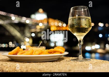 Cena con calamari fritti e vino Porto bianco in un ristorante a Porto vicino al fiume la sera con una bella vista. Foto Stock