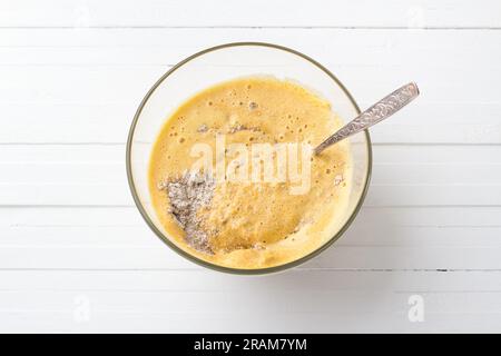 Ciotola di vetro con impasto per frittelle di zucca con farina d'avena su sfondo di legno bianco, vista dall'alto. Fase di cottura del cibo fatto in casa. Foto Stock