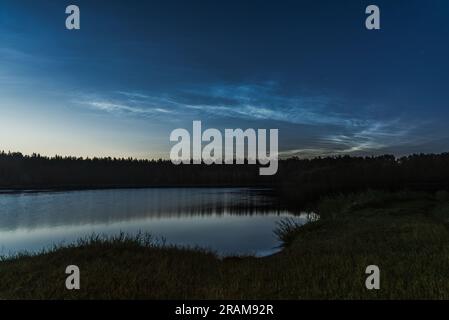 Nubi noctilucent sopra il lago forestale in Lettonia nella notte di luglio Foto Stock