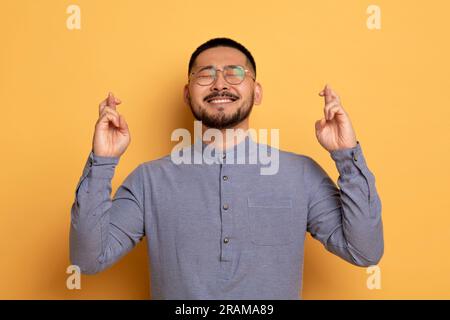 Esprimere un desiderio. Ritratto di un allegro asiatico che tiene le dita incrociate, Foto Stock