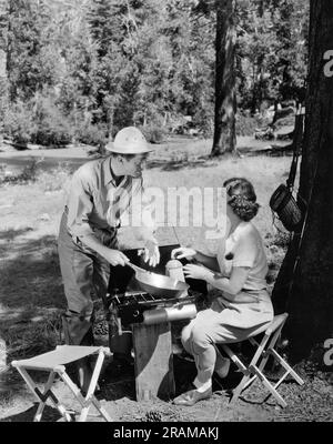 Hollywood, California: c. 1935 attori William Powell e Myrna Loy in una stufa mentre campeggiano in una scena di un film. Foto Stock