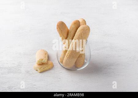 Biscotti savoiardi fatti in casa appena sfornati in una tazza di vetro su un tavolo grigio chiaro. Foto Stock