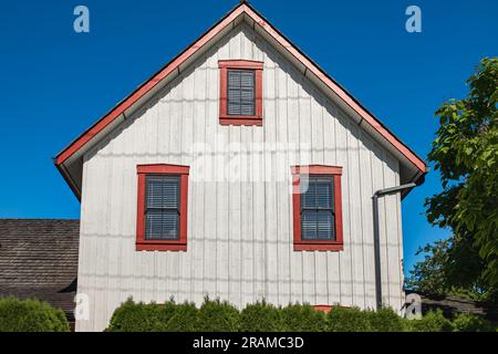 Una bella casa bianca con finestre con persiane a cornice rossa. Tre finestre su un muro di legno in una tradizionale casa americana. Finestre con telaio vintage, Foto Stock