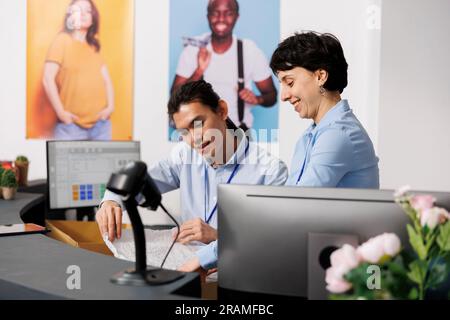 Diversi colleghi che preparano i pacchi per la consegna, in piedi al banco in una moderna boutique. Donna che indossa abiti alla moda in scatole di cartone, che discute del rapporto di spedizione con il centro commerciale Foto Stock