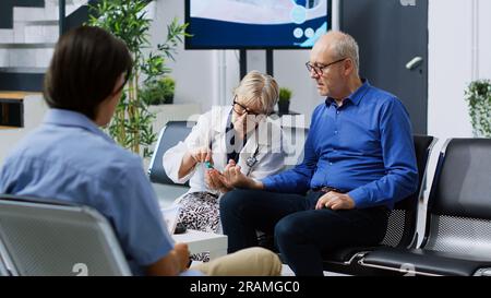 Medic anziano che misura il livello di insulina e glucosio con glucometro, prelevando un campione di sangue durante l'esame con un paziente anziano affetto da diabete. Specialista che fa test medico in sala d'attesa ospedale. Foto Stock