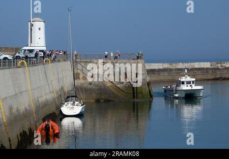 Gita in barca alle Isole farne di ritorno al porto di Seahouses entrando nel porto il 12 giugno 2023 osservata dalle mura del porto da persone vicino alla luce del porto. Foto Stock