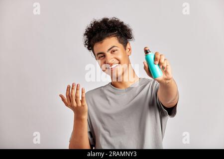 Il giovane con i capelli ricci neri si lava il viso sulle mani, pronto ad affrontare la sua routine quotidiana di cura e cura della pelle. Uomo che si prepara per un buon fac Foto Stock