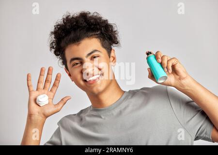 Il giovane con i capelli ricci neri si lava il viso sulle mani, pronto ad affrontare la sua routine quotidiana di cura e cura della pelle. Uomo che si prepara per un buon fac Foto Stock
