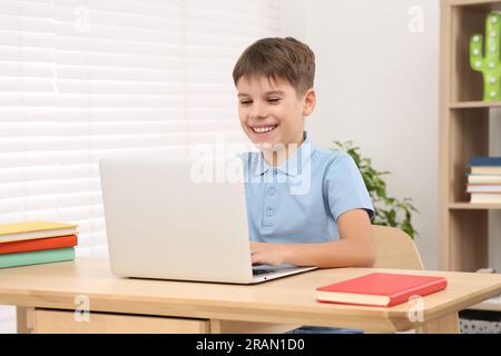 Un ragazzo sorridente che usa il computer portatile alla scrivania in camera. Ambiente di lavoro domestico Foto Stock