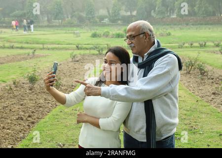 Indiano Joyful Grand father che guarda il cellulare con sua nipote. Sembrano entrambi felici e allegri. Videochiama con la famiglia all'estero. Foto Stock