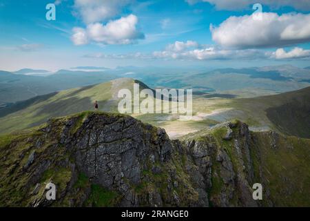 Un panorama aereo che cattura un escursionista in piedi su una cresta di montagna nella natura selvaggia scozzese in un giorno estivo Foto Stock