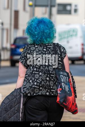 Giovane donna moderna dai capelli blu vivaci che cammina lungo un marciapiede in estate in Inghilterra, Regno Unito. Ritratto. Foto Stock