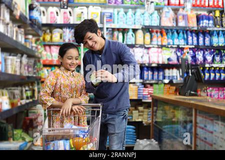 Padre felice con una figlia che acquista in un negozio di alimentari. Comprare della spesa per la casa al supermercato. Analisi del prodotto da acquistare. Prodotto di consumo FMCG Foto Stock