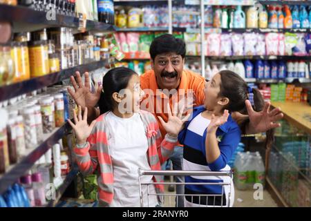 Ragazze adolescenti che comprano generi alimentari al supermercato. I bambini sono stati catturati da mio padre mentre compravano dolci. Momenti divertenti nel negozio al dettaglio locale. Giocare a Nascondi e cerca Foto Stock