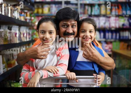 Ritratto di un padre felice indiano che fa shopping in un ipermercato con bambini, acquistando prodotti alimentari in base alle loro esigenze. Foto Stock
