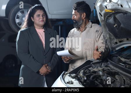 Meccanico in piedi con cliente felice che stringe la mano. Il cliente è soddisfatto di ottenere la consegna in tempo. Rapporto completo sull'auto in mano. Foto Stock