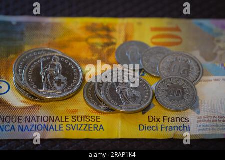 Diverse monete di franchi svizzeri appoggiate su una vecchia banconota. Foto Stock