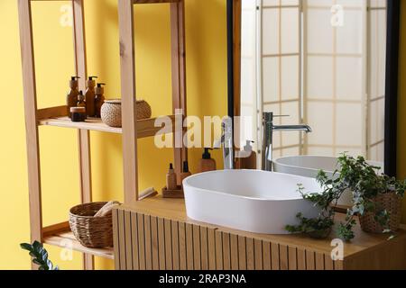 Lavello bianco con accessori per il bagno su cassetti, scaffalature e impianto domestico vicino alla parete colorata Foto Stock