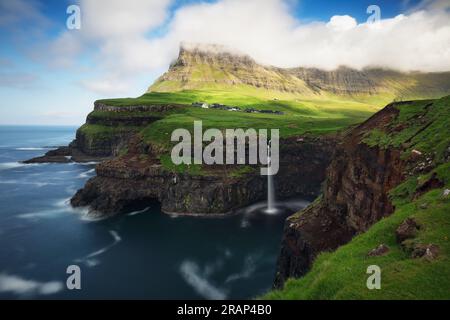 La cascata delle Isole Múlafossur Vágar si trova vicino al villaggio Gasadalurron e all'isola. Verde paesaggio montano caotico. Foto Stock