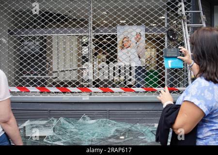 Una donna fa una foto con il suo telefono. Optique, 7 Rue Louise Thuliez, Place de Fêtes, 75019, Parigi, Francia, 30 giugno 2023. Gli ottici ottici vengono attaccati dopo una terza notte di violenze e rivolte per l'uccisione di un adolescente da parte della polizia martedì sera a Nanterre, un sobborgo di Parigi. Crediti: Jane Burke/Alamy Live News. Foto Stock