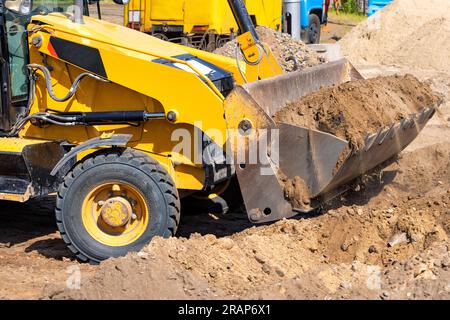 I lavori di terra vengono eseguiti da un bulldozer con trattore gommato utilizzando una grande benna metallica. Foto Stock