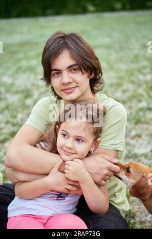 Fratellanza, sorellanza, fratelli, concetto di famiglia. Un giovane fratello amorevole e allegro che abbraccia la sua graziosa sorella sorridente, coccolandosi sullo sfondo esterno. Foto di alta qualità Foto Stock