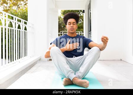 Rilassato uomo birazziale che pratica meditazione yoga seduto sul balcone. Benessere, forma fisica e stile di vita sano, inalterato. Foto Stock
