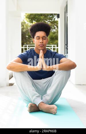 Rilassato uomo birazziale che pratica meditazione yoga seduto sul balcone. Benessere, forma fisica e stile di vita sano, inalterato. Foto Stock
