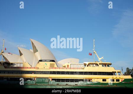 Sydney Opera House e Manly Ferry in giallo e verde, Collaroy, una barca di classe Freshwater passa davanti alle vele bianche del SOH, il cielo blu e le nuvole Foto Stock