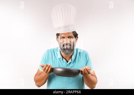 Ritratto di un cuoco indiano barbuto che indossa una t-shirt e un berretto da chef. Espressioni sorridenti su sfondo bianco. Tenere in mano la spatola e il cucchiaio per friggere Foto Stock