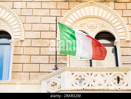 Bandiera tricolore italiana che sventola sul balcone di un edificio istituzionale in stile barocco. Foto Stock