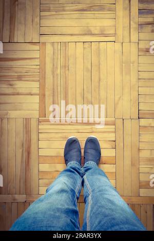 Foto ritagliata di gambe maschili in piedi in sneaker su parquet di legno Foto Stock