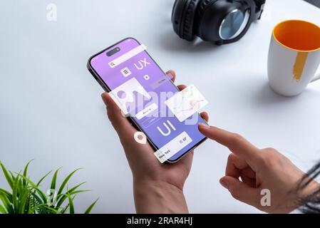 Processo di creazione di un'interfaccia per un'app mobile. Concetto di interfaccia utente ed esperienza. App moderna su smartphone nelle mani di una donna Foto Stock