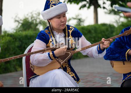 Donna kazaka in costume blu che suona dombra strumento musicale kazako , Almaty, Kazakistan. 25 maggio 2023 Foto Stock
