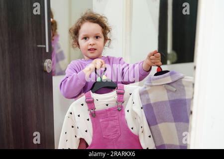 Una bambina simpatica sceglie un abito nello spogliatoio del negozio Foto Stock