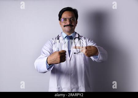 Indiano fiducioso Dottore tenendo in mano una bevanda salutare e suggerendo di bere fresco e sano. Il medico in piedi su uno sfondo bianco. Foto Stock
