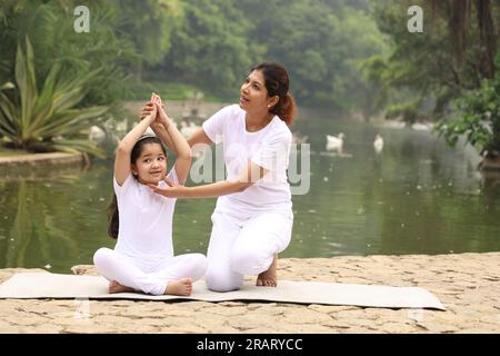 Mamma sana che insegna Yoga pone in ambiente sereno verde la mattina presto nel parco per mantenere uno stile di vita sano. Giornata internazionale di yoga. Foto Stock