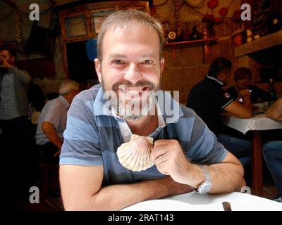 Ragazzo sorridente caucasico che tiene un capesante al tavolo di un ristorante Foto Stock