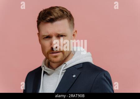 Un uomo confuso con un abito casual si disgusta, sospetta qualcosa di brutto, isolato su uno sfondo rosa polveroso Foto Stock