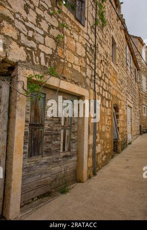 Una strada di case storiche in pietra nel villaggio di Milna sulla costa occidentale dell'isola di Brac in Croazia. Le case in primo piano sono abbandonate Foto Stock