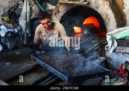 Na'im Sharab, un palestinese di 70 anni, possiede il forno primitivo più antico ereditato dai suoi antenati 130 anni fa. Lui, i suoi figli e nipoti lavorano nel forno nella città di Gaza. Sharab dice che lavorano ogni mattina per preparare il forno, che funziona su legna e olio bruciato acquistato da negozi che sostituiscono gli oli per le auto. Con la crisi dell'elettricità e del gas, alcune persone si sono abituate a inviare pane, caffè e pentole al forno, dove la maggior parte delle pentole da cucina viene prodotta durante l'Eid al-Adha a causa della disponibilità di carne in grandi quantità. Palestina. Foto Stock