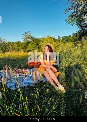 Il paradiso del pittore: La donna con un abito giallo e un cappello crea arte durante un picnic. Foto Stock