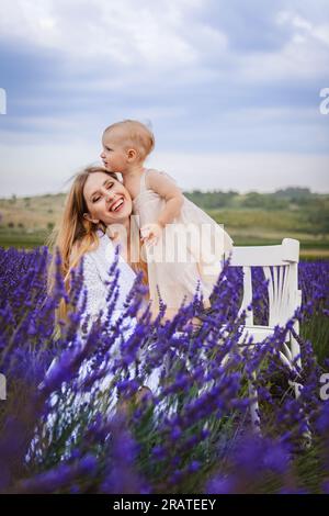 Questo è un momento felice quando una madre abbraccia sua figlia mentre è seduta in un campo di lavanda, la ragazza è in piedi su una sedia bianca Foto Stock