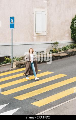 Donna alla moda che attraversa il roadm indossando un cardigan a maglia lunga Foto Stock