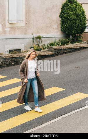 Donna alla moda che attraversa il roadm indossando un cardigan a maglia lunga Foto Stock