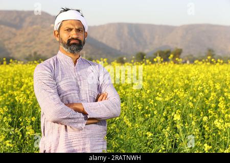 Agricoltore che si sente orgoglioso del suo impegno per la crescita del suo campo. Bellissimo ritratto di un contadino rurale indiano in piedi nel campo di senape. Foto Stock