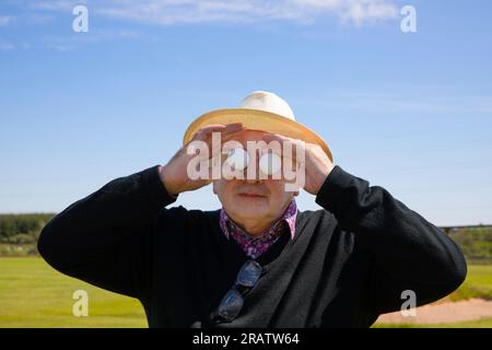 L'uomo anziano tiene le palle da golf davanti agli occhi sullo sfondo di un campo da golf. Concetto di golf pazzo, pazzo di golf o di golf pazzo. Foto Stock