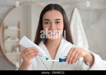 Una giovane donna che spreme dentifricio dal tubo allo spazzolino elettrico in bagno Foto Stock