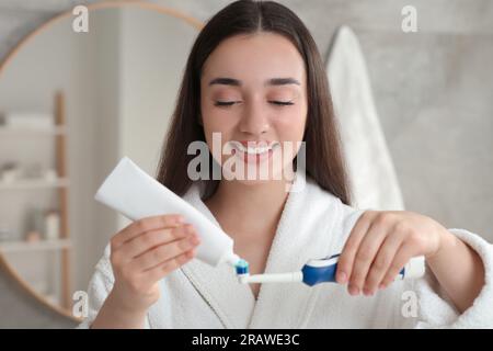 Una giovane donna che spreme dentifricio dal tubo allo spazzolino elettrico in bagno Foto Stock